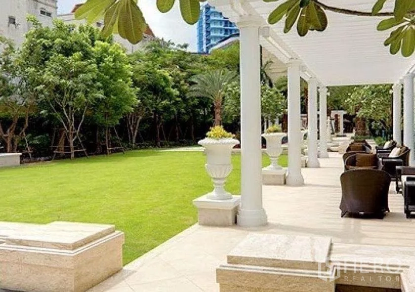 Condominium for sale in Watthana, Bangkok - Shaded terrace with columns, seating area and green lawn in the communal garden.
