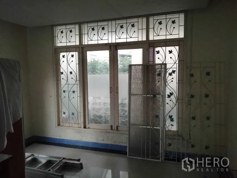 独立式住宅 出售在Prawet, Bangkok - 带大窗与装饰铁艺护栏的房间，墙边有梯子。