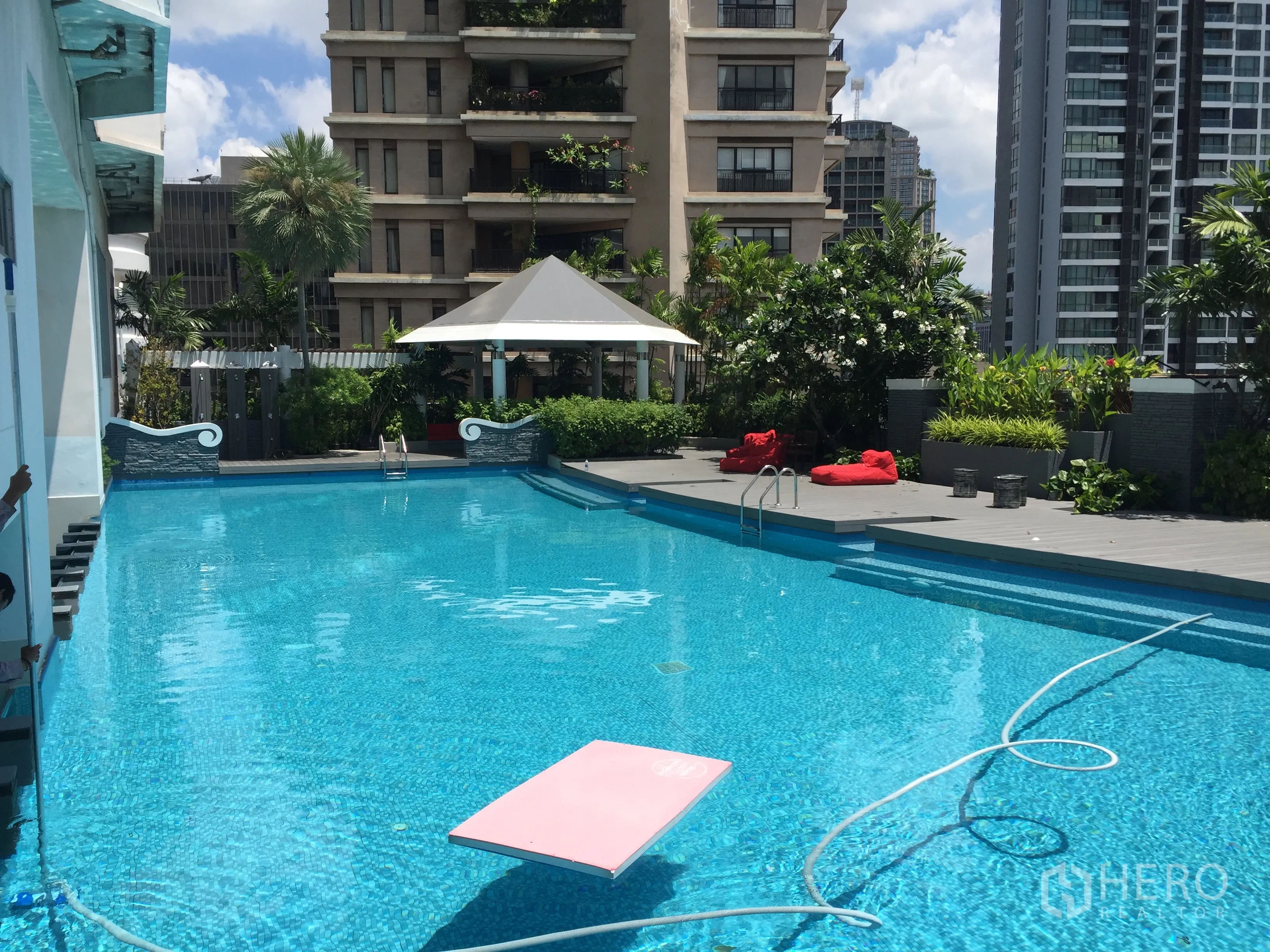 Condominium for rent in Khlong Toei, Bangkok - Condominium outdoor swimming pool with sun deck, greenery and city buildings.