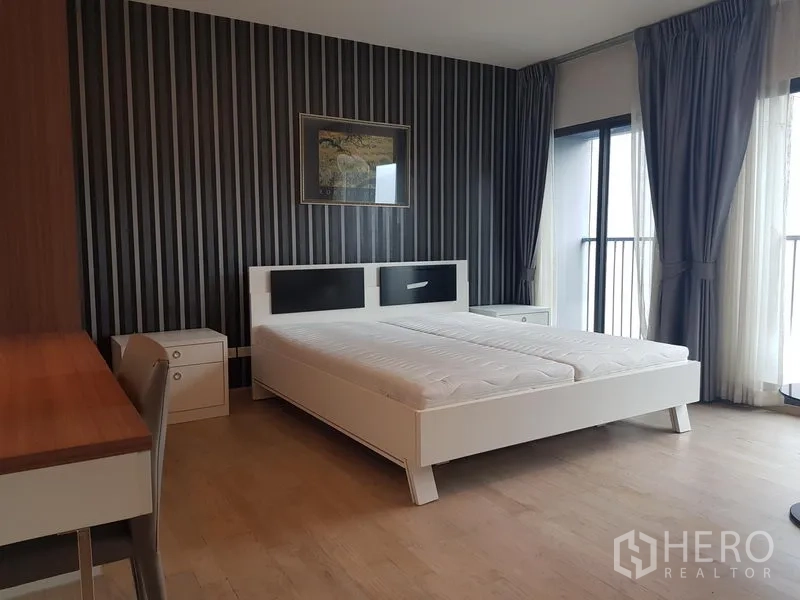 Condominium for rent in Khlong Toei, Bangkok - Master bedroom with striped feature wall, large windows and balcony access.