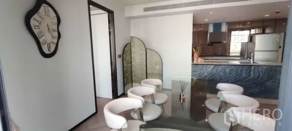 公寓 出租在Watthana, Bangkok - 餐区配弧形餐椅与装饰屏风，对面是带大理石风岛台的厨房。