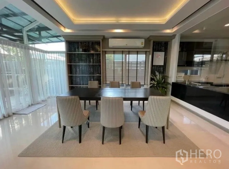 Detached House for rent or sale in Bang Phli, Samut Prakan - Dining area for six with striped chairs, built-in shelving, air conditioning and sheer curtains.