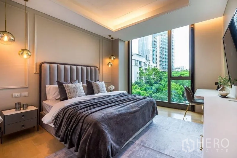 Condominium for rent in Pathum Wan, Bangkok - Master bedroom with floor-to-ceiling windows, upholstered headboard, pendant lights, and green city views.