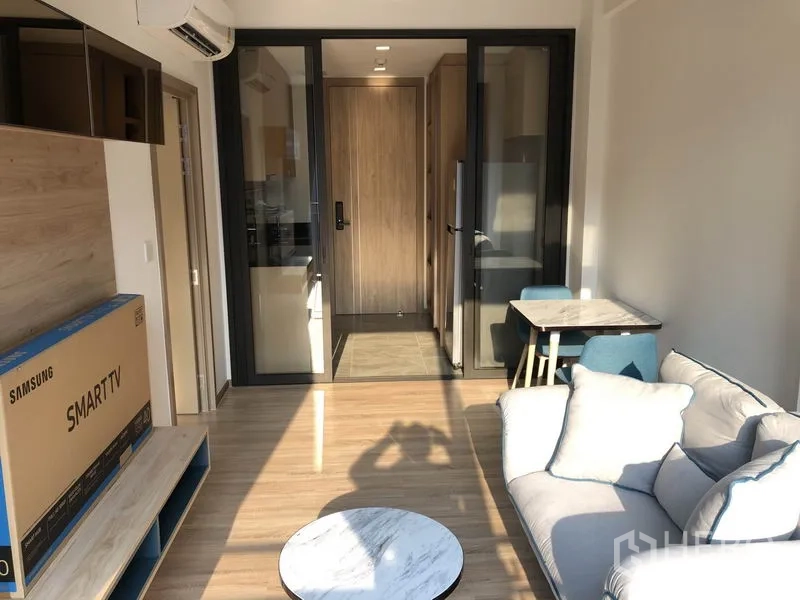 Condominium for rent in Watthana, Bangkok - Bright living room with sofa, TV console, and sliding glass doors to the kitchen and entry in a modern Bangkok condo.