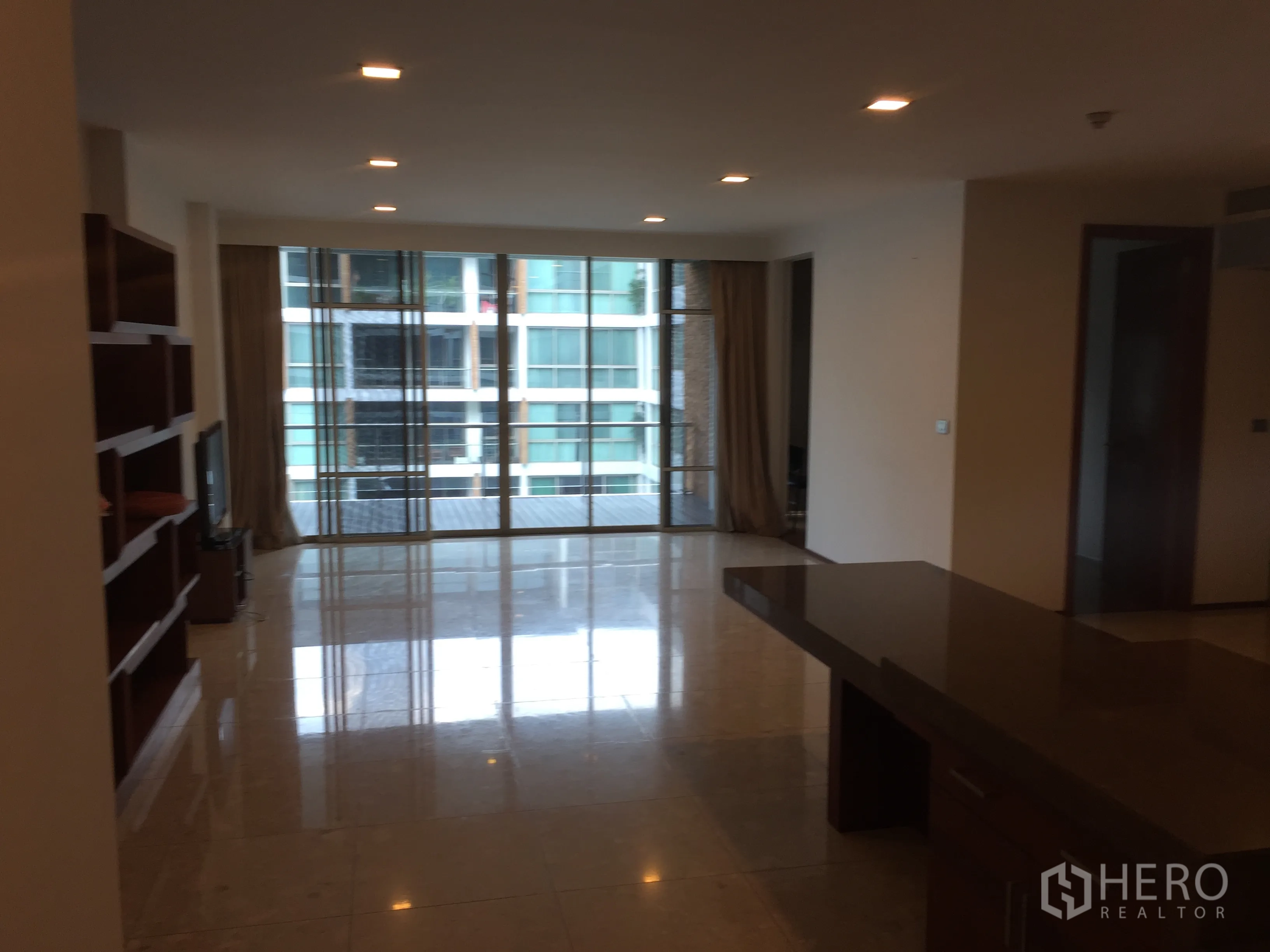 Condominium for rent in Khlong Toei, Bangkok - Open-plan living and dining area with marble floors, recessed lighting, and floor-to-ceiling windows to the balcony.