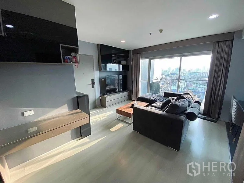 คอนโด ขายในHuai Khwang, Bangkok - ห้องนั่งเล่นสว่าง โซฟาตัวใหญ่ ผนังทีวี และประตูกระจกสไลด์ออกไประเบียงวิวเมือง