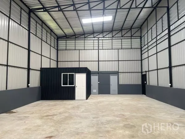 Warehouse for rent in Wang Thonglang, Bangkok - Spacious high-ceiling warehouse interior with steel trusses, skylight panel, and a built-in office room.