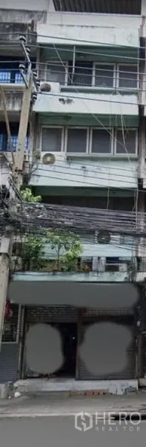 Shophouse for sale in Watthana, Bangkok - Four-storey shophouse exterior in Bangkok with roller shutter frontage, balconies, and street power lines near Ekkamai BTS.