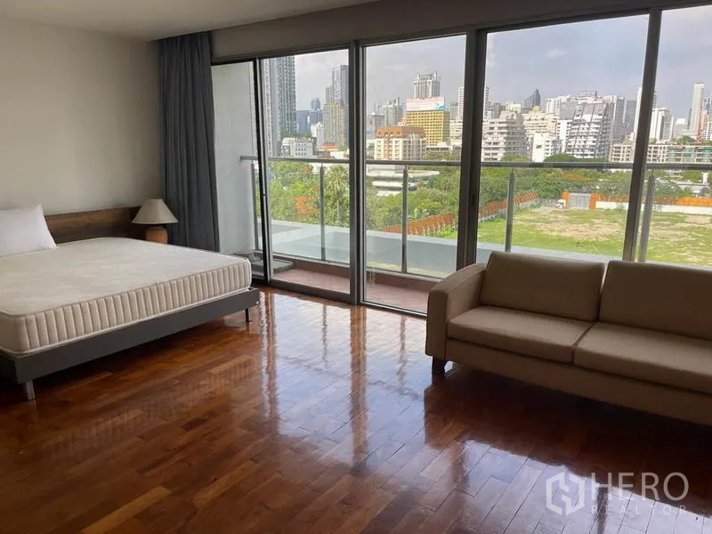 公寓 出租在Pathum Wan, Bangkok - 大卧室配沙发与大床，通过落地门欣赏城市与绿地景观。