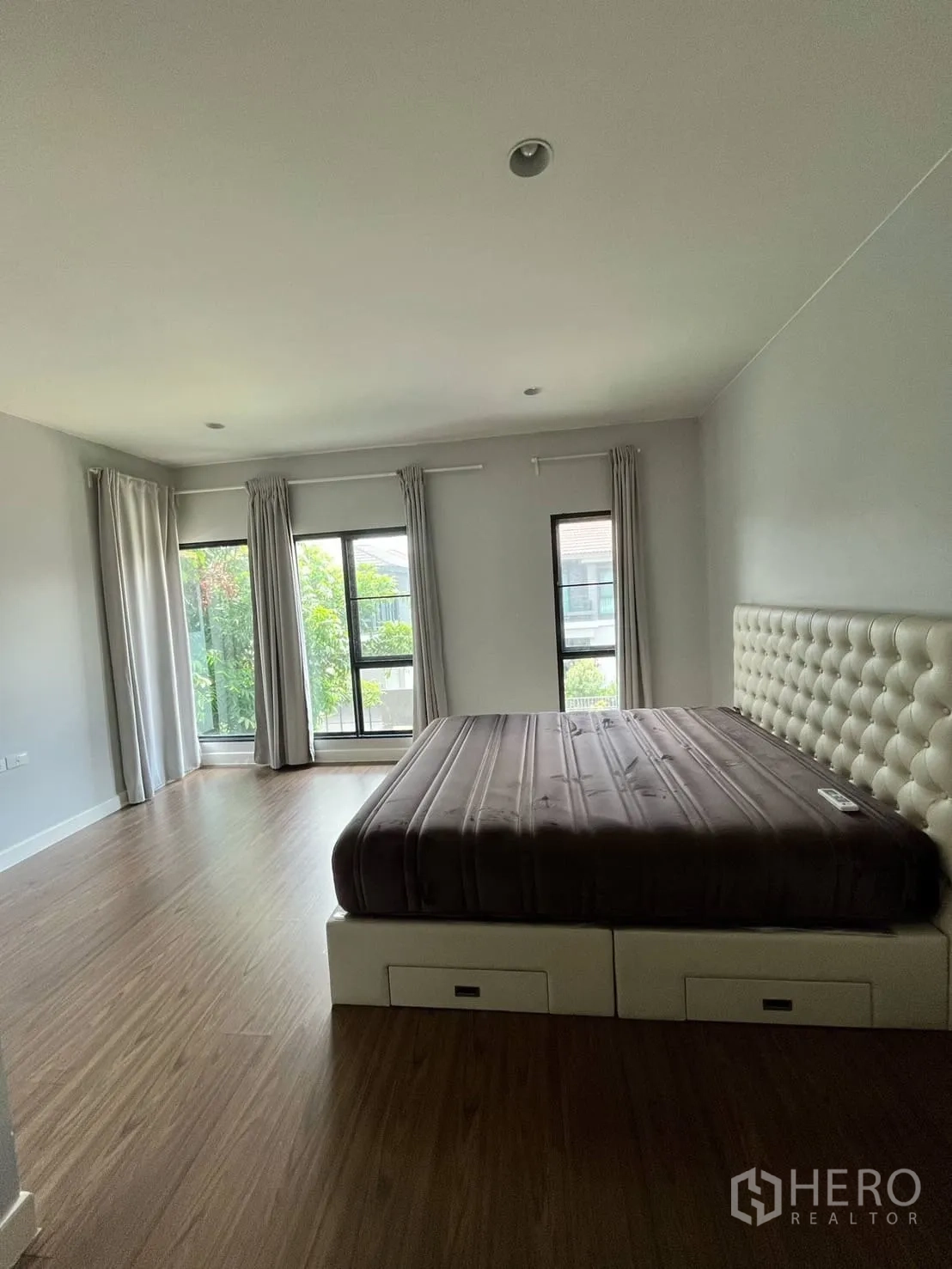 Detached House for rent or sale in Lam Luk Ka, Pathum Thani - Spacious bedroom with large windows, curtains and wood floors.