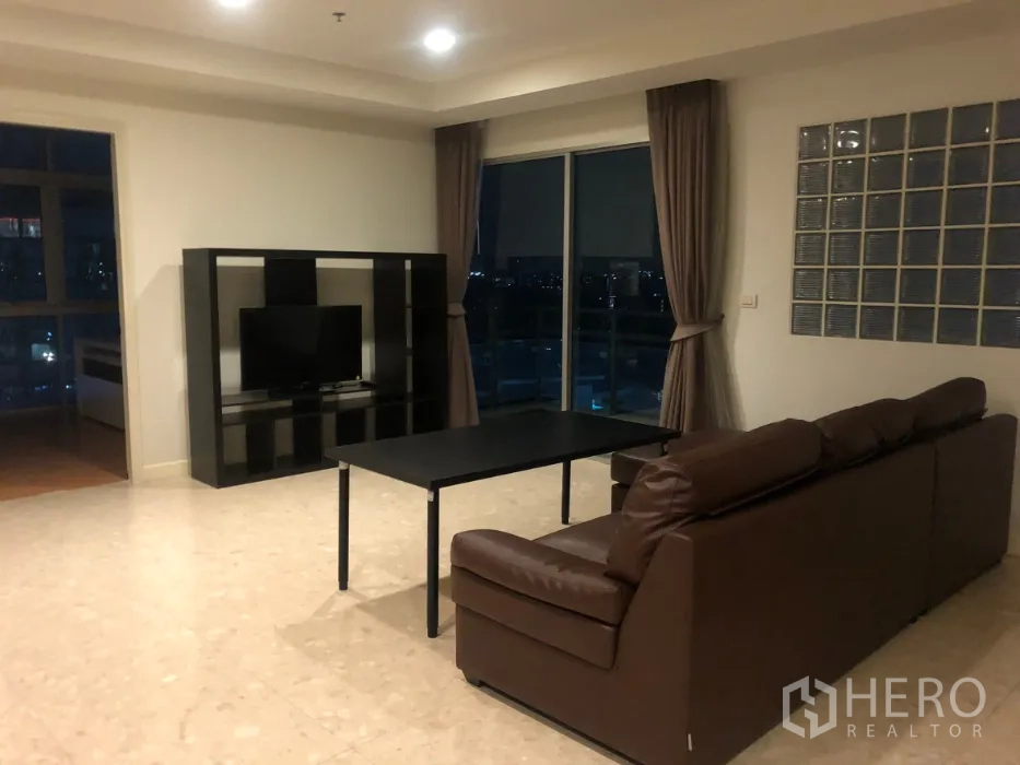 公寓 出售在Khlong Toei, Bangkok - 宽敞客厅，棕色皮沙发、电视柜，大幅窗户望向夜景