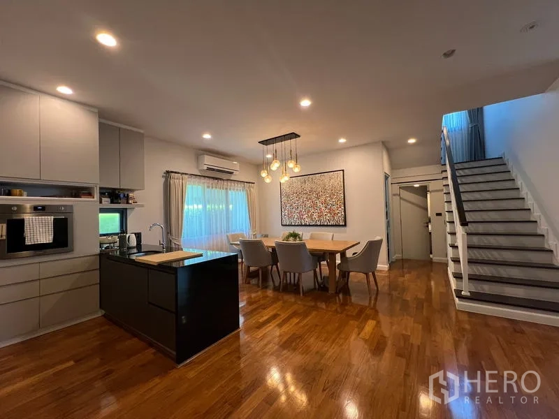 Detached House for rent in Bang Kapi, Bangkok - Open-plan dining area with island kitchen and staircase, warm wooden floors.