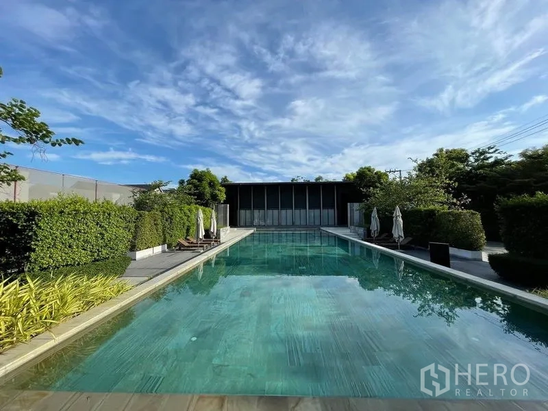 Detached House for sale in Sai Mai, Bangkok - Long rectangular outdoor swimming pool with deck chairs and manicured hedges.