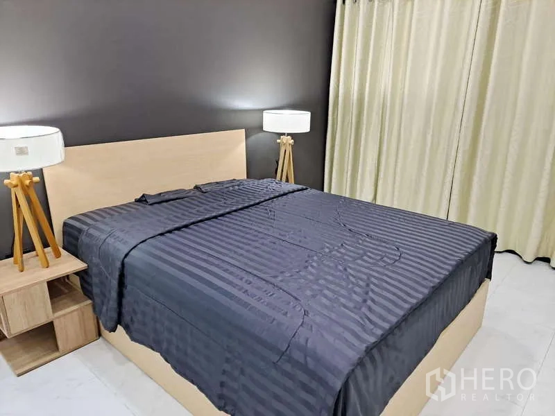 公寓 出租在Khlong Toei, Bangkok - 深灰床品的双人床，两侧为三脚落地灯，墙面为灰色。