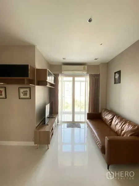 Condominium for rent in Phra Khanong, Bangkok - Sunlit living room with brown leather sofa, TV unit and balcony doors.
