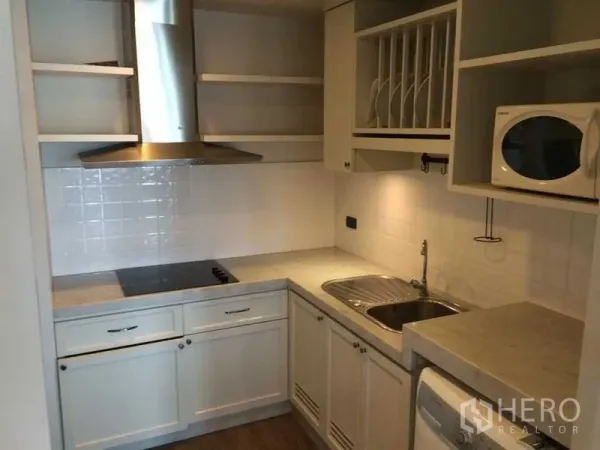 Condominium for rent in Khlong Luang, Pathum Thani - U-shaped kitchen with white cabinets, range hood, electric cooktop, sink and microwave at Nusasiri Grand Condo near BTS Ekkamai.