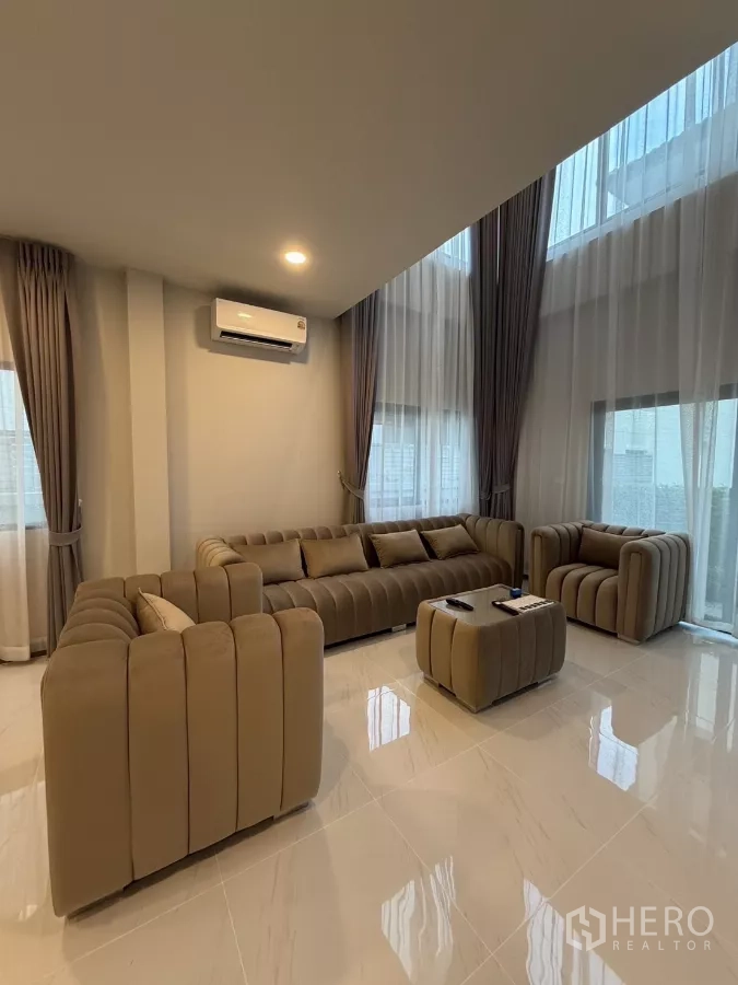 独立式住宅 出租在Bang Phli, Samut Prakan - 挑高客厅，大窗采光，L形沙发与亮面地砖。