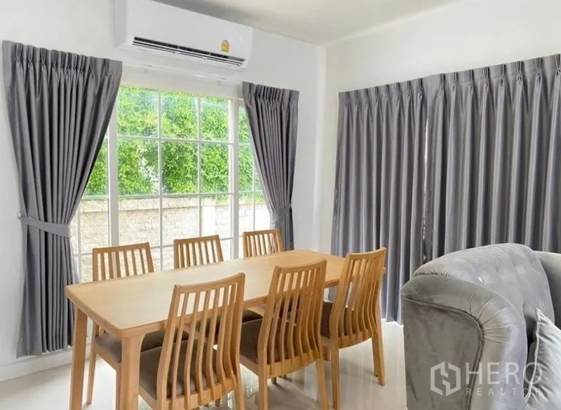 บ้าน ให้เช่าหรือขาย - ห้องทานอาหาร โต๊ะไม้ 6 ที่นั่ง ข้างหน้าต่างบานใหญ่ พร้อมเครื่องปรับอากาศและผ้าม่านสีเทา.