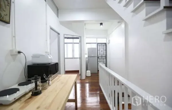 Home Office for rent in Khlong Toei, Bangkok - Bright corridor with pantry table, white railing, and timber floors leading to multiple rooms.