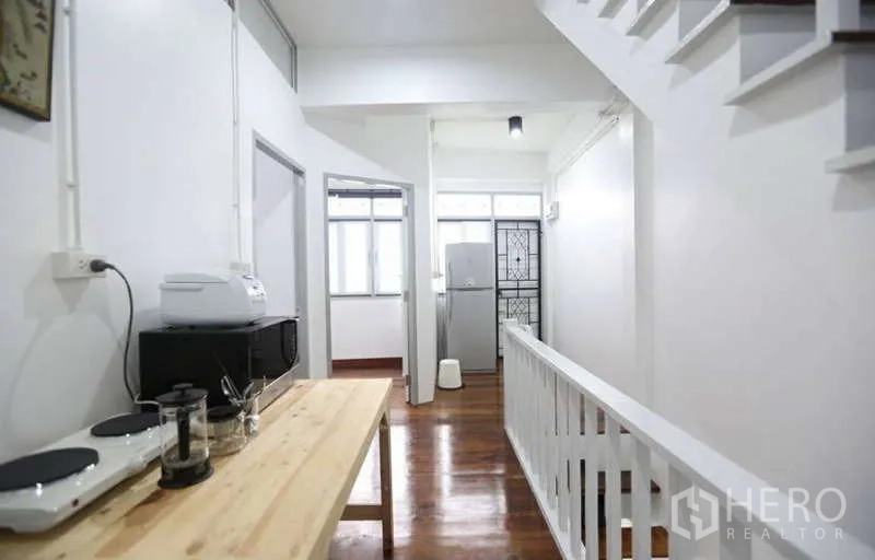 Home Office for rent in Khlong Toei, Bangkok - Bright corridor with pantry table, white railing, and timber floors leading to multiple rooms.