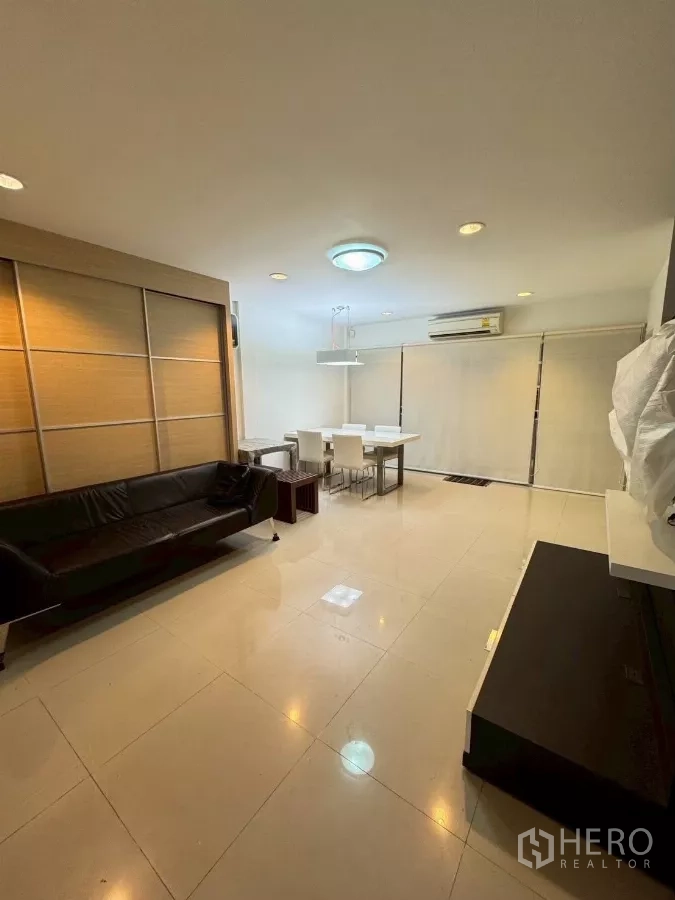 Townhouse for rent in Suan Luang, Bangkok - Spacious living room with glossy tiles, sofa and dining set with window blinds.