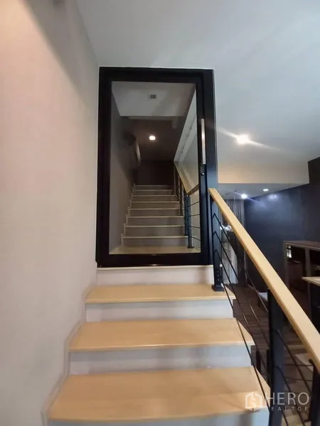 Townhouse for rent in Suan Luang, Bangkok - Close-up of staircase with light wood steps, metal handrail and framed glass door.