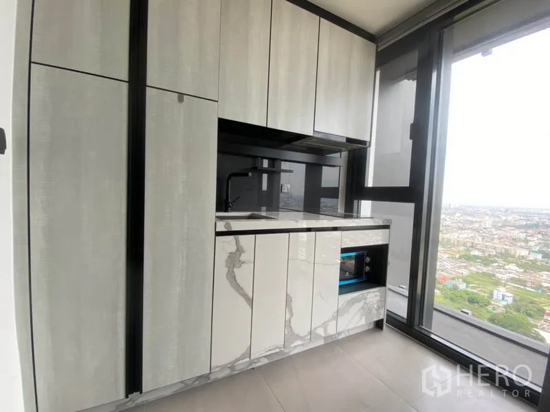 Condominium for rent in Phra Khanong, Bangkok - Compact modern kitchen with marble-look cabinetry beside a large window overlooking the Bangkok skyline.