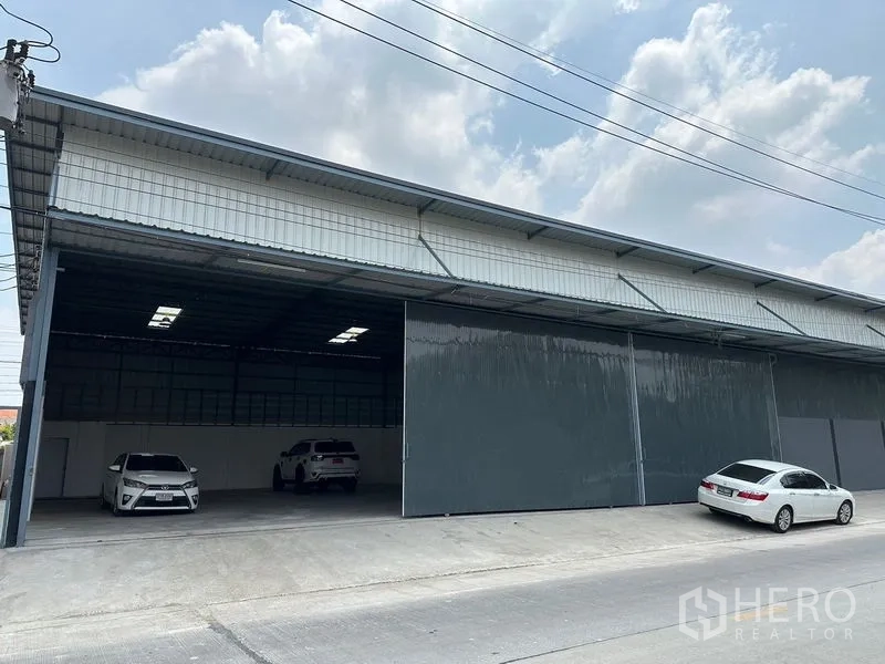 Warehouse for rent in Lam Luk Ka, Pathum Thani - Partially open bay revealing covered parking and a wide driveway in front of the warehouse.