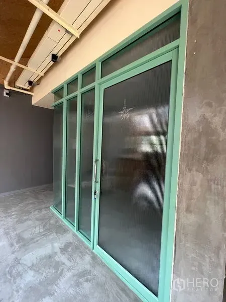 Retail Space for rent in Watthana, Bangkok - Close-up of mint-green framed glass storefront door and panels beneath exposed ceiling pipes.