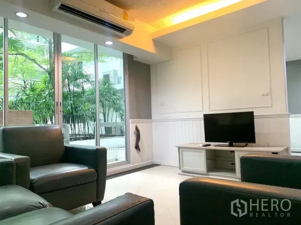 公寓 出租在Khlong Toei, Bangkok - 客厅设电视柜与皮沙发，推拉落地窗通向面向花园的阳台。