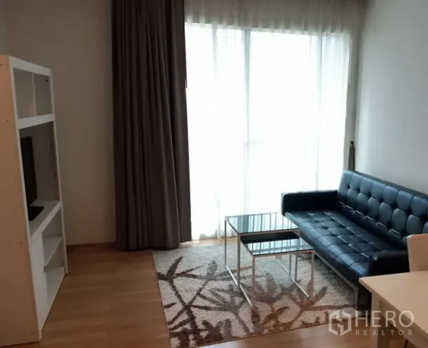 Condominium for rent in Khlong Toei, Bangkok - Bright living room with a black leather sofa, glass coffee tables, TV shelf and floor-to-ceiling window with curtains.