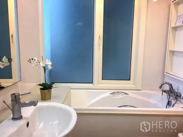 Condominium for rent in Khlong Toei, Bangkok - Bright bathroom with white vanity, soaking bathtub, and frosted window.