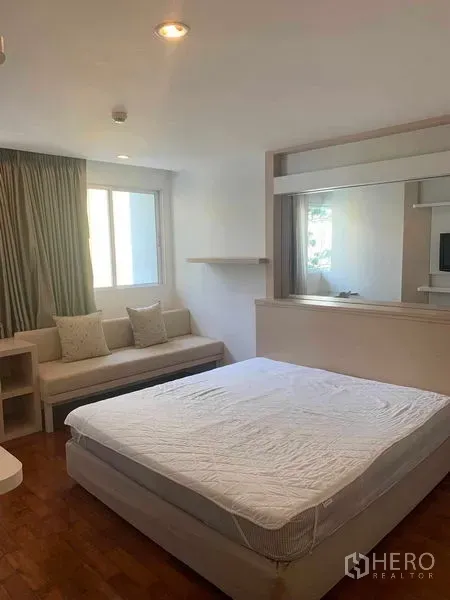 Condominium for rent or sale in Khlong Toei, Bangkok - Spacious bedroom featuring a large bed, sofa bench, and wide windows.