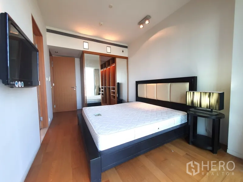 Condominium for rent in Sathon, Bangkok - Primary bedroom with hardwood floors, wall-mounted TV and mirrored wardrobe.