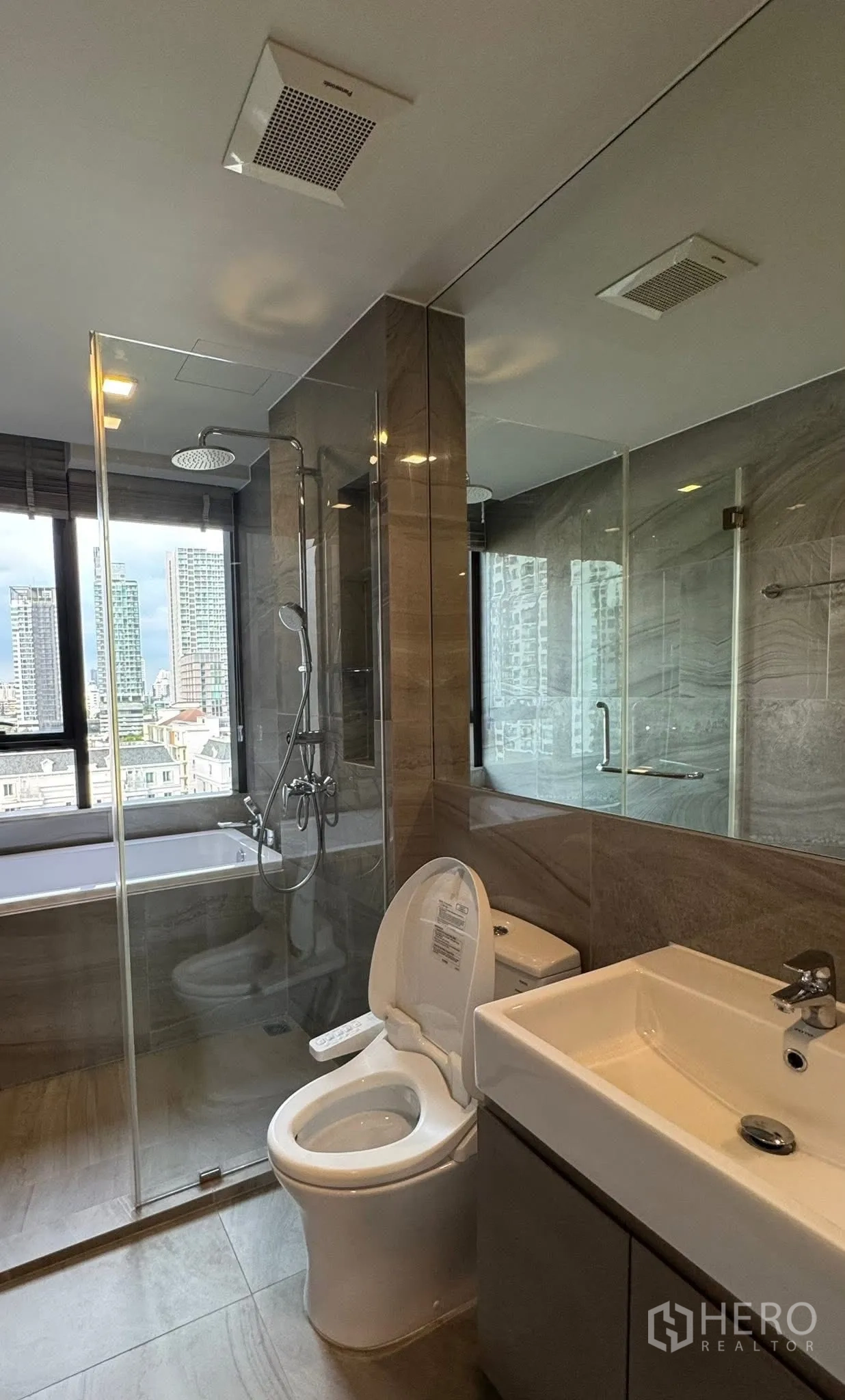 Condominium for rent in Khlong Toei, Bangkok - Bathroom with rain shower and bathtub beside a window overlooking the skyline.