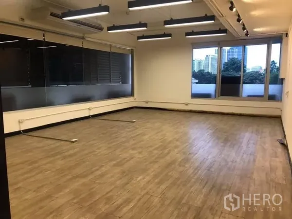 Office Space for rent in Khlong Toei, Bangkok - Corner office area with large windows, city views, wood-look floors, and linear pendant lighting.