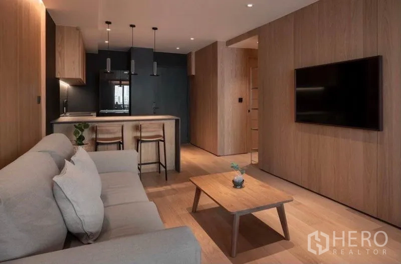 Condominium for rent in Phaya Thai, Bangkok - Open-plan living area facing a modern kitchen with island, pendant lights and a wall-mounted TV.
