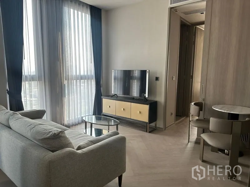 Condominium for rent - Cozy living room setup with sofa, TV and sheer curtains filtering daylight.
