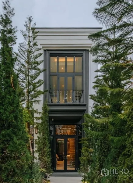 Detached House for sale in Saphan Sung, Bangkok - Elegant narrow entry building framed by evergreen trees and a small balcony above.
