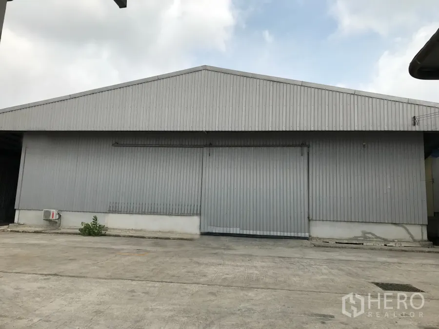 Warehouse for rent in Mueang Samut Prakan, Samut Prakan - Front view of corrugated metal warehouse with large sliding door and wide concrete yard in Samut Prakan.