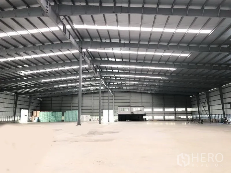 Factory for rent in Bang Phli, Samut Prakan - Wide interior view of the warehouse showing central steel columns and an office block at the rear.