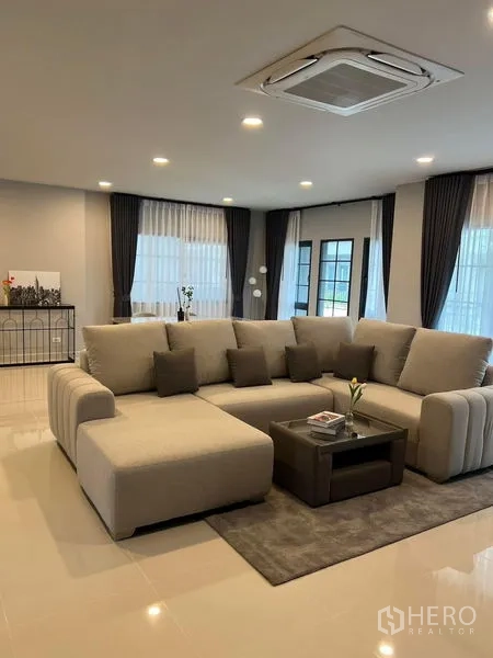 独立式住宅 出租在Bang Phli, Samut Prakan - 宽敞客厅，大型转角沙发、吊顶天花机与亮面地砖。