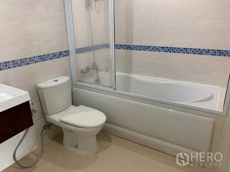 Condominium for rent in Bang Rak, Bangkok - Bathroom featuring bathtub with glass screen, toilet and blue mosaic border tiles.