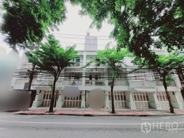 店屋 出租在Bang Rak, Bangkok - 临街多层商铺式立面，带阳台与折叠门，行道树成荫。
