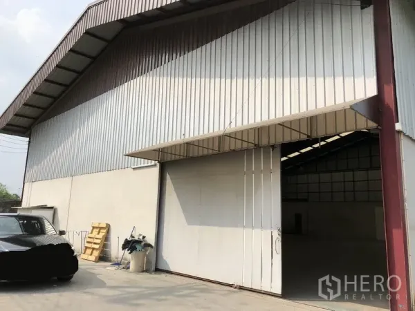 Warehouse for rent in Bueng Kum, Bangkok - Exterior of a metal-clad warehouse in Bueng Kum with a wide sliding door and forecourt parking.