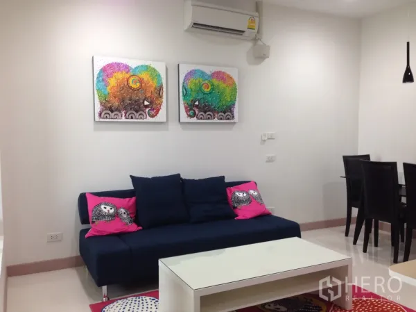 Condominium for rent in Phaya Thai, Bangkok - Bright lounge with navy sofa, colorful artwork, white coffee table and a dining set for four.