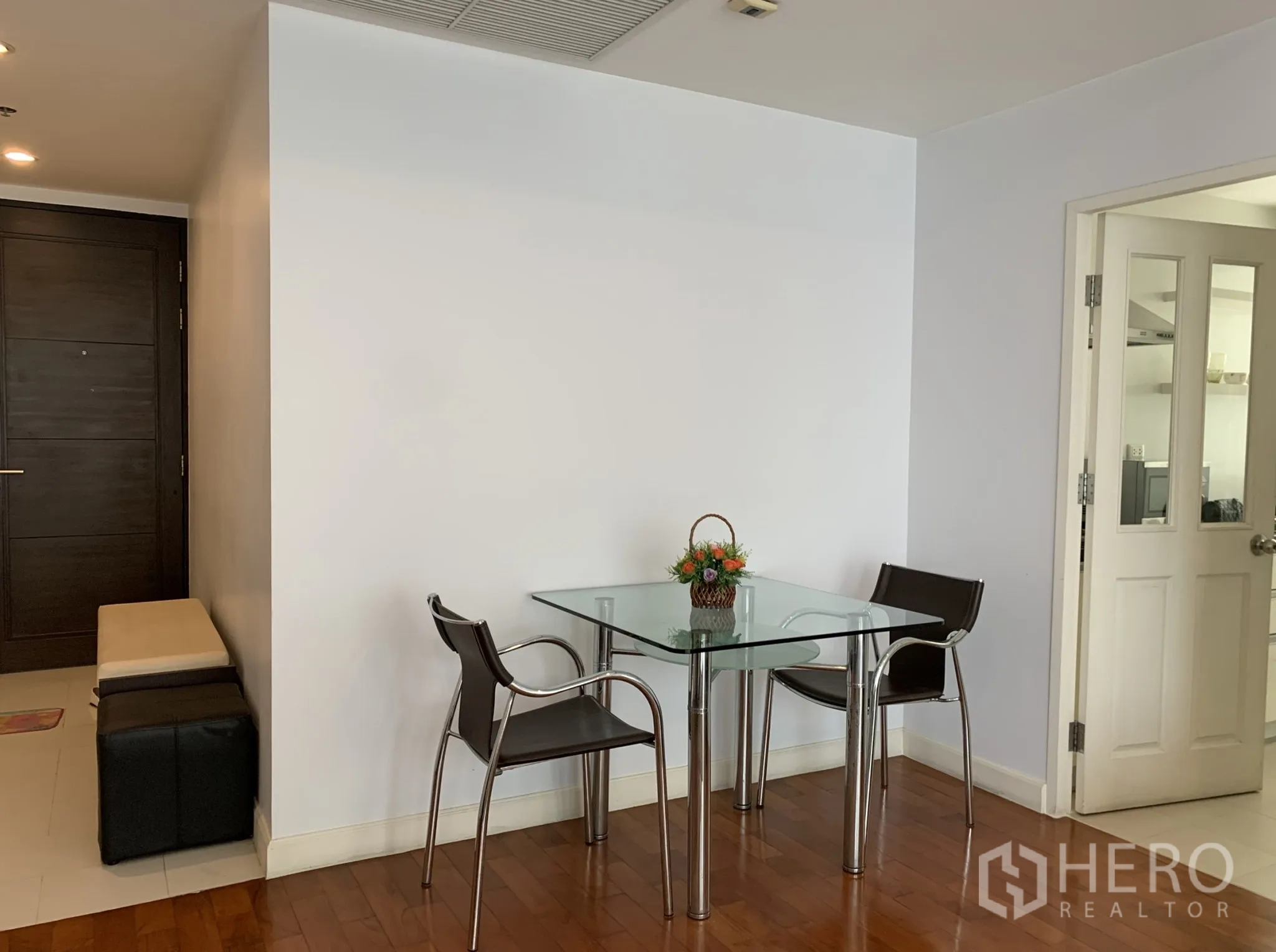 Condominium for rent in Khlong Toei, Bangkok - Compact dining corner with a glass-top table and two modern chairs next to the kitchen door.