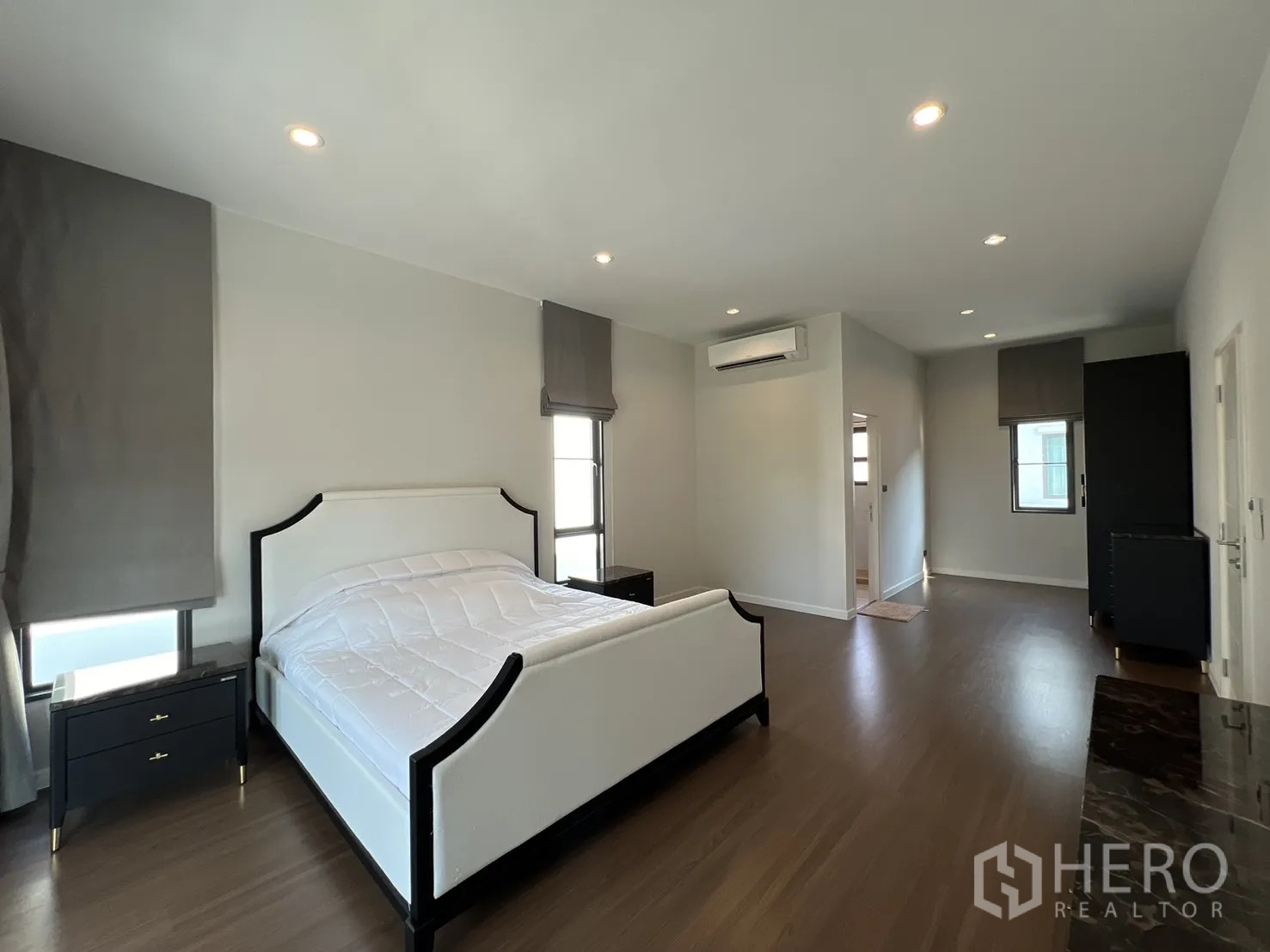 Detached House for rent in Bang Phli, Samut Prakan - Spacious master bedroom with white bed, wood floors, air conditioner and side tables.