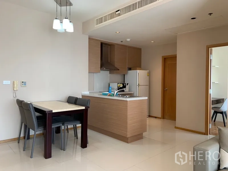 Condominium for rent in Khlong Toei, Bangkok - Open-plan kitchen with island, built-in cabinets and a four-seat dining table in a modern condo.