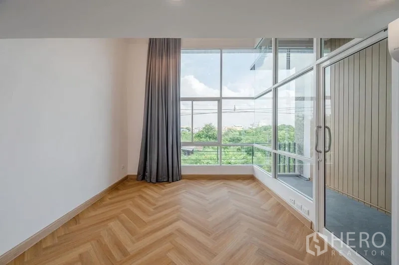 联排别墅 出售在Lat Phrao, Bangkok - 卧室带大面积玻璃与窗帘，可通往小阳台，景观绿意。